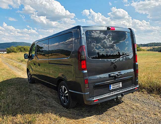 Dark grey Renault Trafic minibus, rear three-quarter view, parked in a countryside field