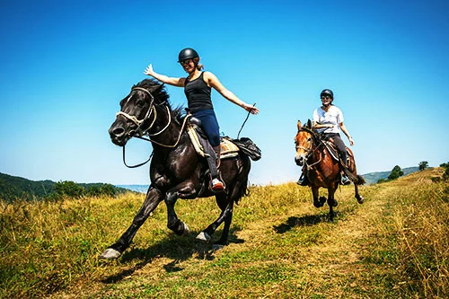 Two riders on horseback crossing a green mountain meadow near Teteven, Bulgaria